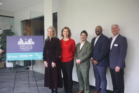 A picture of the Employee Ownership Raleigh Sign with the following people standing next to it from left to righ: Mayor of Raleigh, Janet Cowell, Illa Burbank Executive Director at North Carolina Employee Ownership Center, Zen Trenholm, Director of Employee Ownership Cities Program and Policy at the Democracy at Work Institute (DAWI), Julian McKinley Co-executive Director at the Democracy at Work Institute (DAWI), Mark Weldon Small Business Development Manager